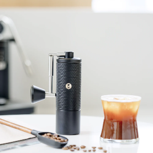 timemore chestnut c5 series handkaffeemühle auf einem Tisch neben Eiskaffee und Kaffeebohnen – Coffee Coaching Club